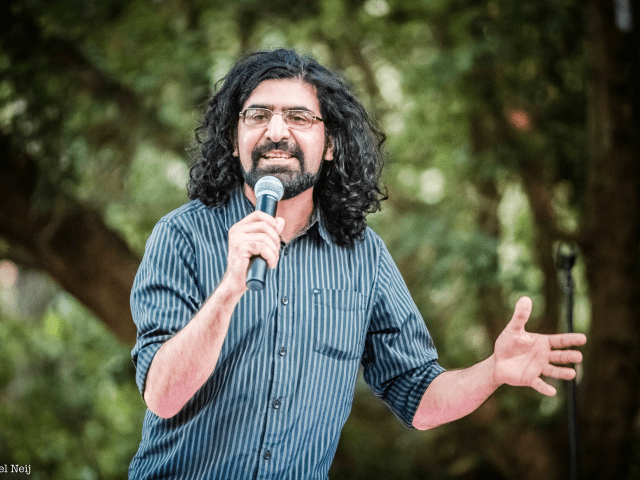 Comedian Hermes Ahmadi a man standing in front of a tree holding a microphone